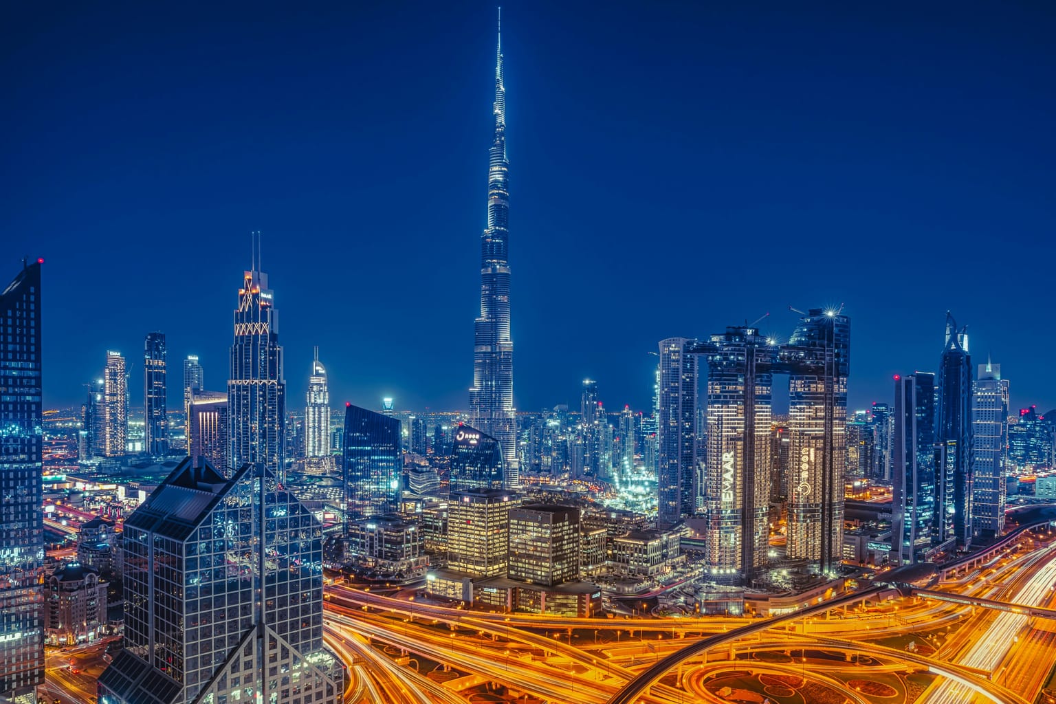 A night view of Dubai's skyline with illuminated skyscrapers and busy highways.